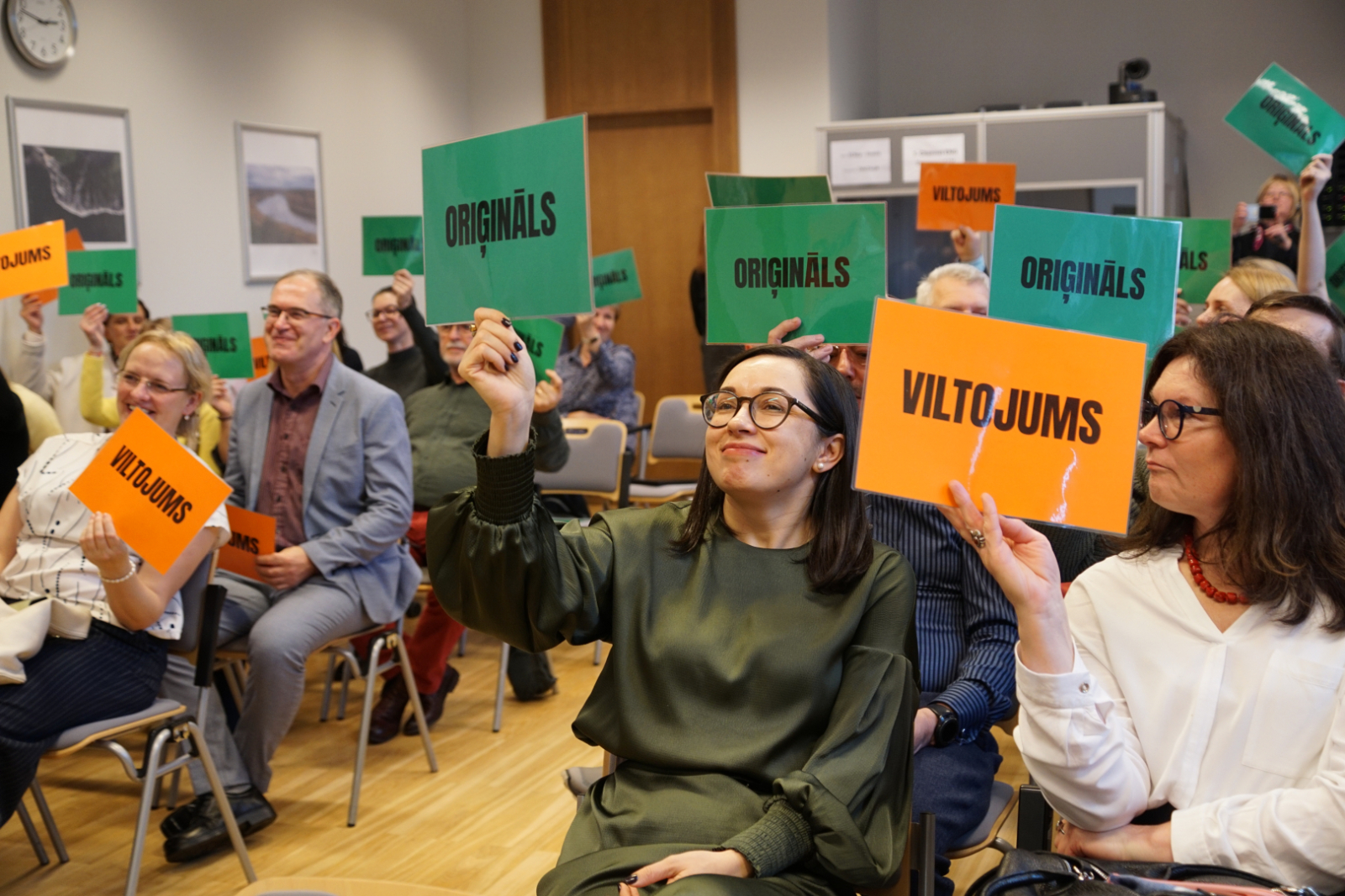 Muitas semināra 2025 dalībnieki turot rokā spēles kartītes 