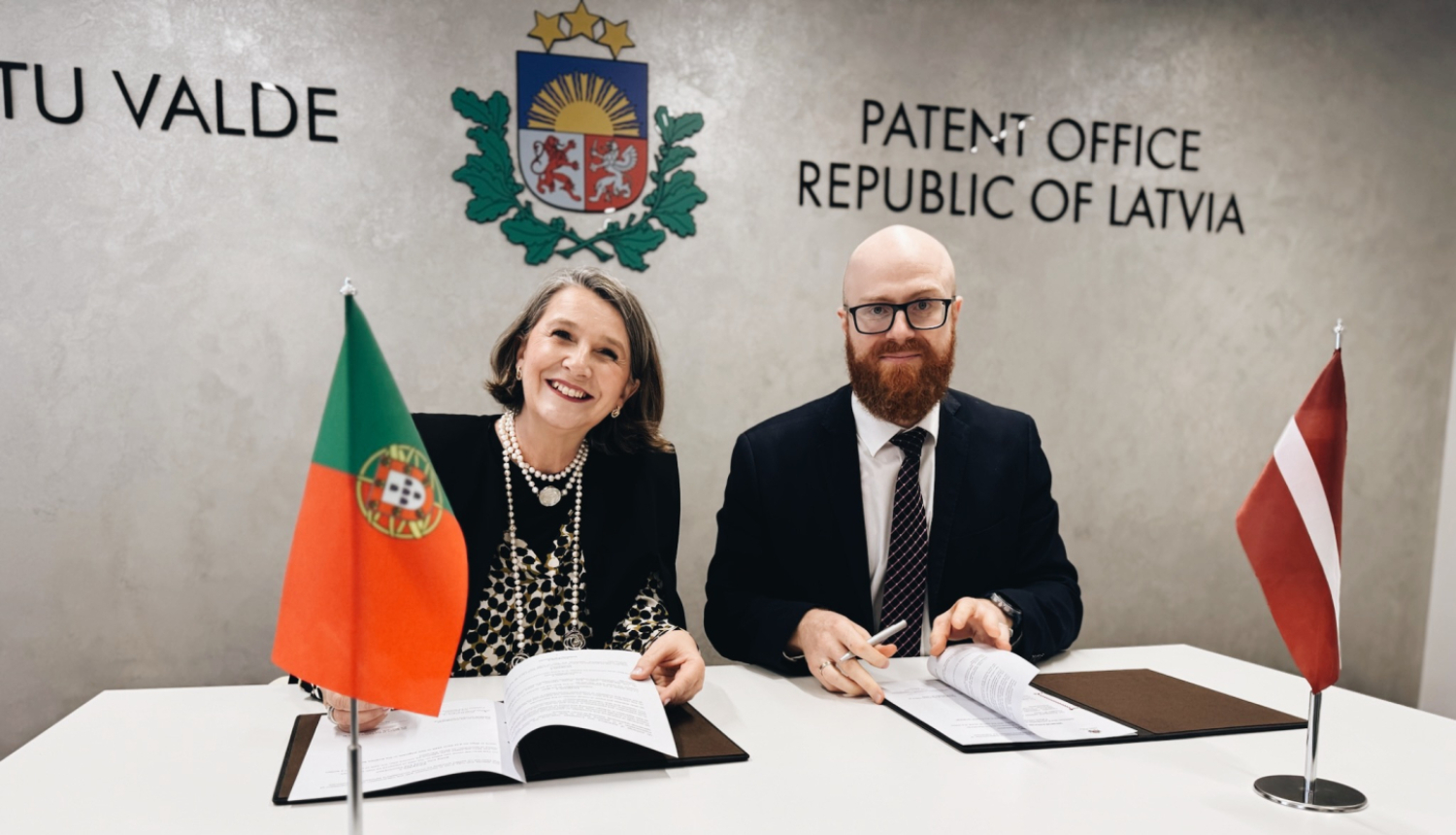 Patentu valdes direktors Agris Bataluaski sēžot pie galda, paraksta divpusēju sadarbības memorandu ar Portugāles Intelektuālā īpašuma iestādes direktori