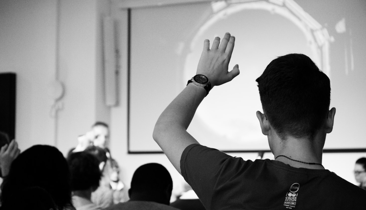 diskusijas dalībnieks pacēlis roku jautājumam (skats no aizmugures)